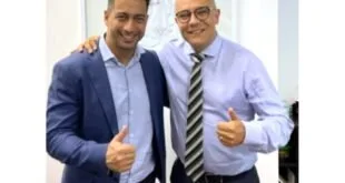 Dois homens de camisa social lado a lado, sorrindo e fazendo sinal de positivo