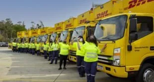 Fila de caminhões amarelos da DHL com trabalhadores de colete refletivo enfileirados