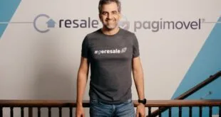Homem de camiseta escura sorrindo diante de parede com os logotipos 'resale' e 'pagimovel'