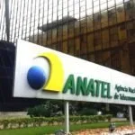 Letreiro da Anatel na entrada de prédio, com painel de vidro ao fundo