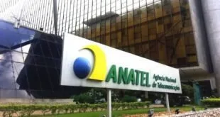 Letreiro da Anatel na entrada de prédio, com painel de vidro ao fundo