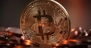 Moeda dourada de bitcoin em pé sobre pilha de moedas em fundo escuro