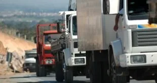 Caminhões brancos e vermelhos enfileirados em rodovia, vistos de frente