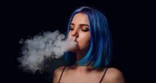 Jovem de cabelo azul soltando fumaça pela boca em fundo preto
