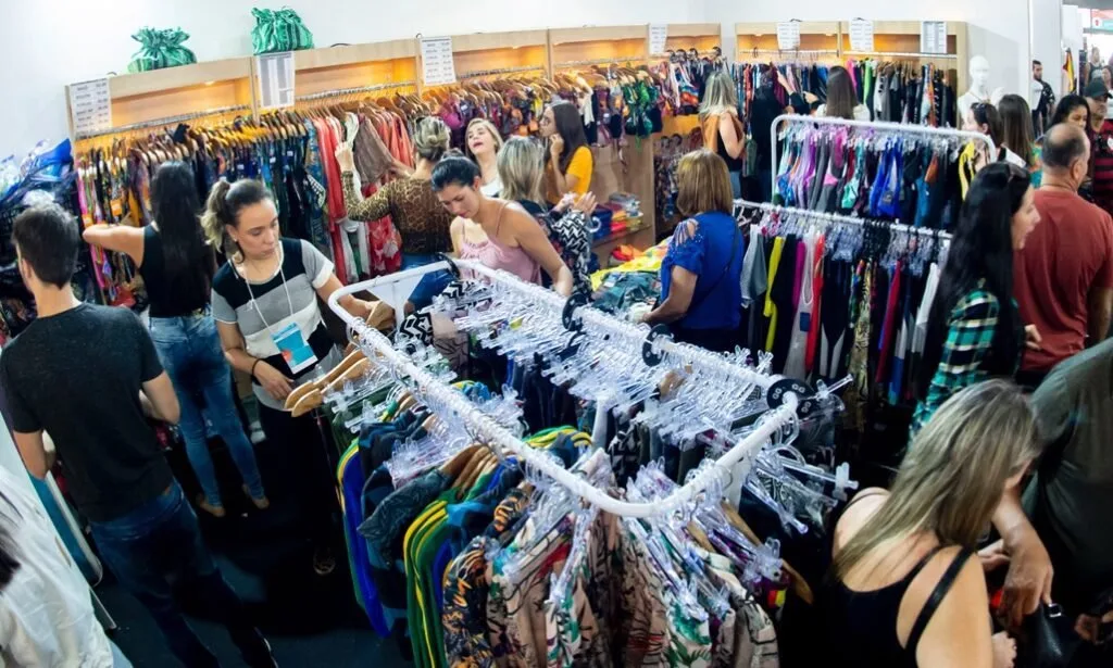 Público circulando entre araras de roupas em feira de confecção