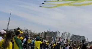 Esquadrilha aérea solta fumaça verde e amarela sobre multidão vestida de amarelo