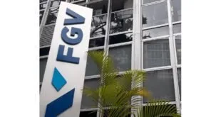 Totem com o logotipo FGV diante de prédio de vidro cercado por plantas