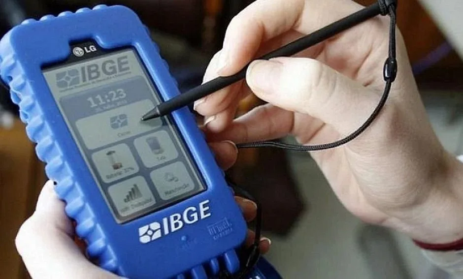 Mão segurando coletor de dados azul com a marca IBGE e caneta digital
