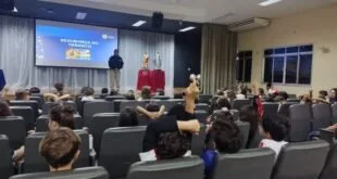 Palestrante uniformizado fala em auditório para plateia de estudantes sentados