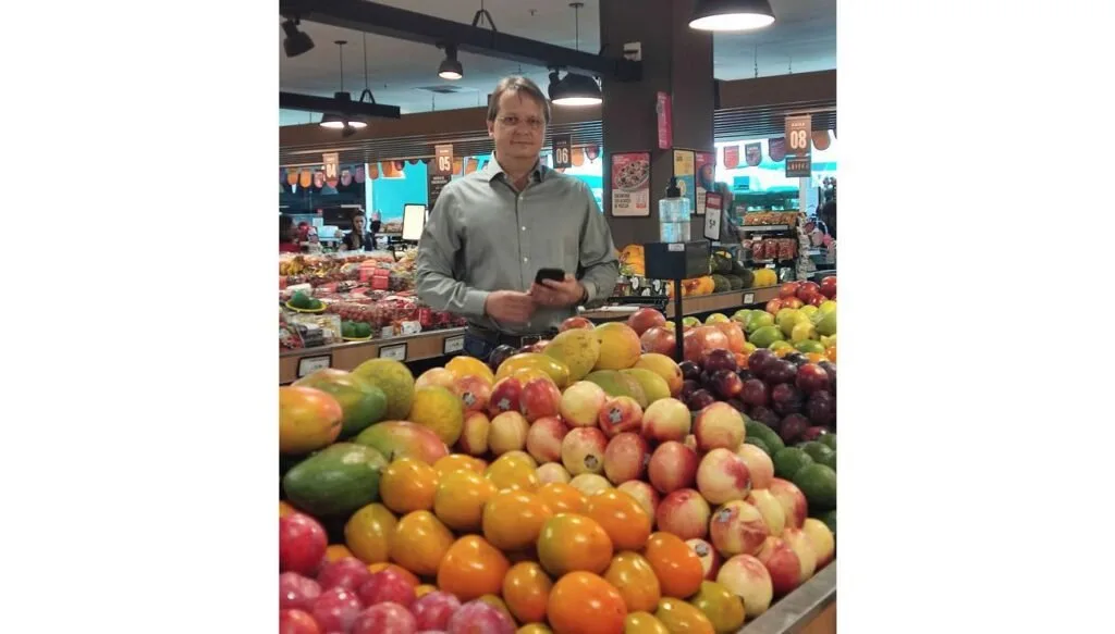 Homem de pé atrás de uma banca de frutas e verduras em mercado