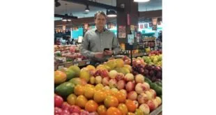 Homem de pé atrás de uma banca de frutas e verduras em mercado