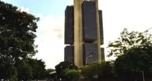 Edifício modernista de concreto e vidro visto da rua com carros passando em avenida