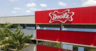 Fachada vermelha de prédio industrial com o logotipo Docile e palmeiras ao redor