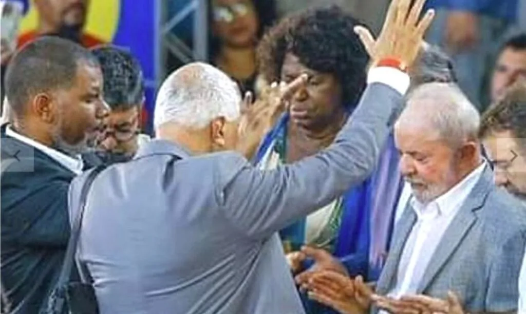 Homem de terno impõe as mãos sobre fiel durante culto com braços erguidos ao fundo