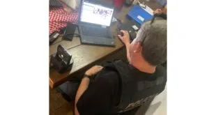 Agente com colete da Polícia Federal analisa notebook sobre mesa durante operação