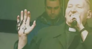Homem com colarinho clerical segura terço e canta ao microfone