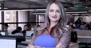 Mulher sorridente segura pasta azul em escritório com estações de trabalho ao fundo