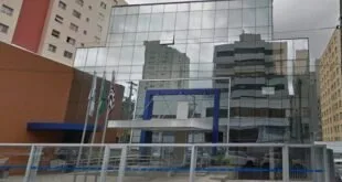 Prédio de fachada espelhada refletindo edifícios vizinhos sob céu nublado