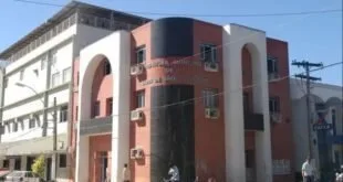 Fachada de prédio público em tons de vermelho e branco com pessoas na calçada