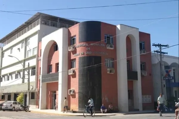 Fachada de prédio público em tons de vermelho e branco com pessoas na calçada