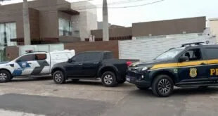 Viaturas da Polícia Militar e da PRF ao lado de caminhonete preta em frente a casa