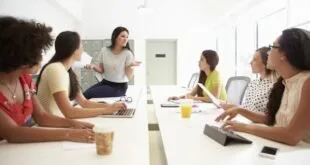 Grupo de mulheres reunidas em torno de mesa de escritório durante reunião de trabalho