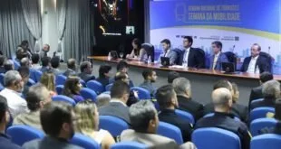 Autoridades sentadas à mesa de abertura de evento diante de plateia em auditório