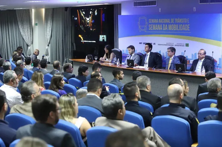 Autoridades sentadas à mesa de abertura de evento diante de plateia em auditório