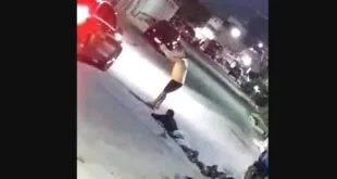 Cena noturna desfocada de rua com pessoa em pé entre veículos e público