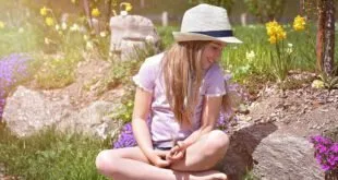 Menina de chapéu de palha sentada sobre uma mala em jardim florido