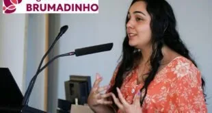 Mulher fala ao microfone diante de painel com a palavra 'Brumadinho'