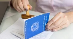 Carimbo sendo aplicado sobre carteira de trabalho azul aberta em uma mesa
