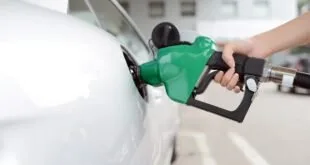Mão segura bico de bomba verde para abastecer um carro branco em posto