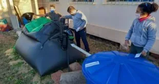 Estudantes manuseiam composteira e caixa d'água azul no quintal de uma escola