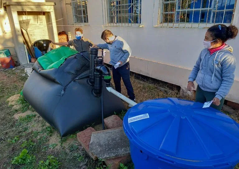 Estudantes manuseiam composteira e caixa d'água azul no quintal de uma escola