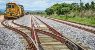 Trilhos de ferrovia com desvio em meio à vegetação sob céu nublado