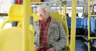 Homem idoso de cachecol sentado no banco de um ônibus segurando um cartão