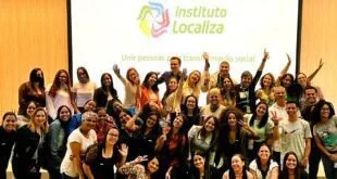 Grupo de pessoas com os braços erguidos posa diante de painel do Instituto Localiza