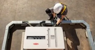 Técnico de capacete branco trabalha sobre inversor solar instalado em telhado