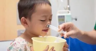 Criança recebe lavagem nasal com seringa enquanto segura uma tigela amarela