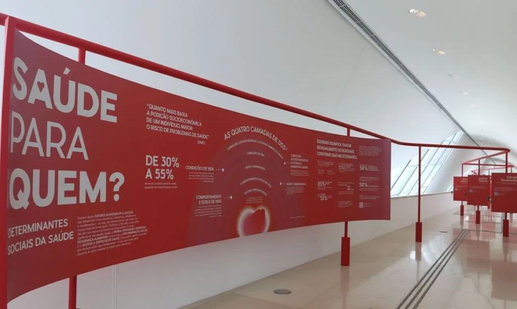 Painel vermelho com textos e gráficos em curva ocupa a parede de um corredor de museu