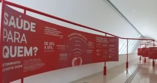 Painel vermelho com textos e gráficos em curva ocupa a parede de um corredor de museu