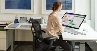 Mulher sentada em cadeira de escritório trabalhando em computador com planilha na tela