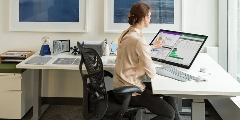 Mulher sentada em cadeira de escritório trabalhando em computador com planilha na tela
