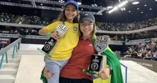 Duas skatistas com medalhas e troféus enroladas em bandeira do Brasil dentro de arena