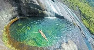 Pessoa nadando em piscina natural de água esverdeada entre paredões de rocha