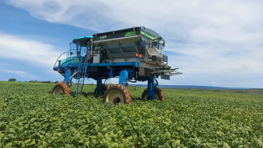 Pulverizador agrícola azul em lavoura de soja sob céu com nuvens