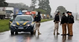 Policiais armados e viatura em bloqueio de rodovia sob chuva