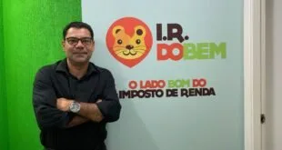 Homem de braços cruzados diante de parede com o logotipo 'I.R. do Bem'