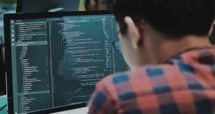 Pessoa de costas diante de monitor com linhas de código em ambiente escuro
